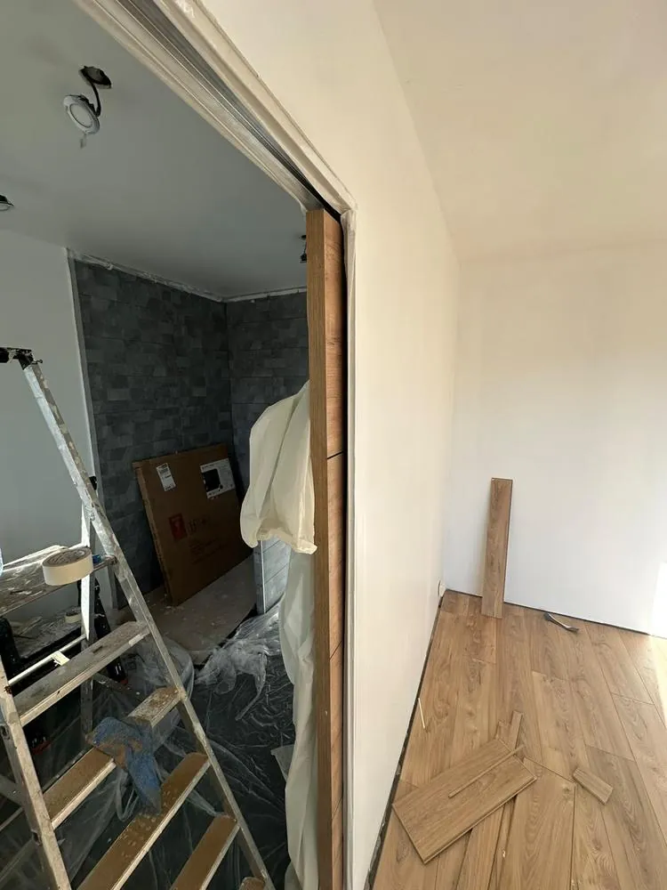 Nouvelle pièce avec sol stratifié et porte coulissante en cours de pose, ouvrant sur une salle d'eau